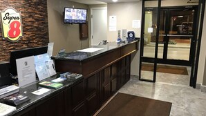 A hotel reception area with a reception desk, a monitor displaying security footage, a sign for 'Super 8', and a door marked 'EXIT'.