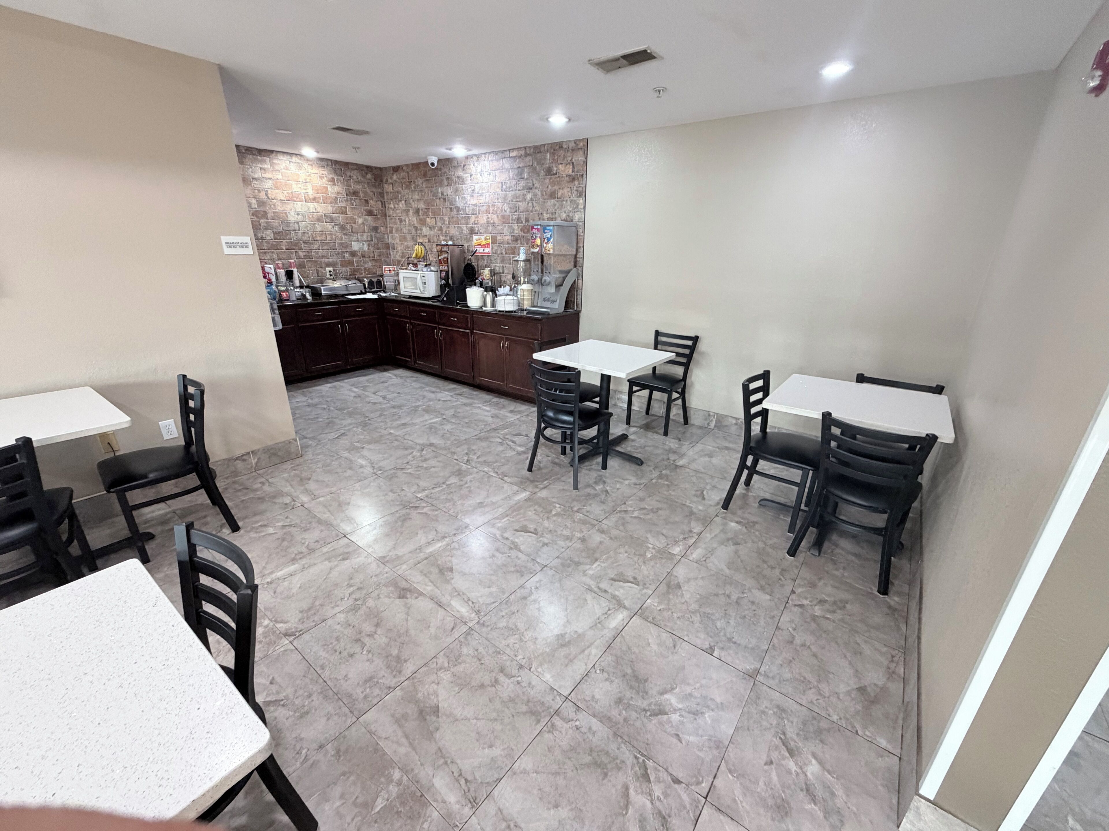 Uma área de refeições com mesas e cadeiras, uma cozinha com eletrodomésticos, e uma parede de pedra.