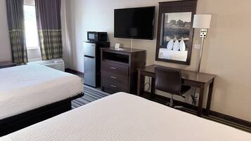 A hotel room with two beds, a desk, a television, and a mirror reflecting a cityscape.