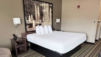A hotel room with a large bed, a nightstand, a lamp, and a wall-mounted artwork.