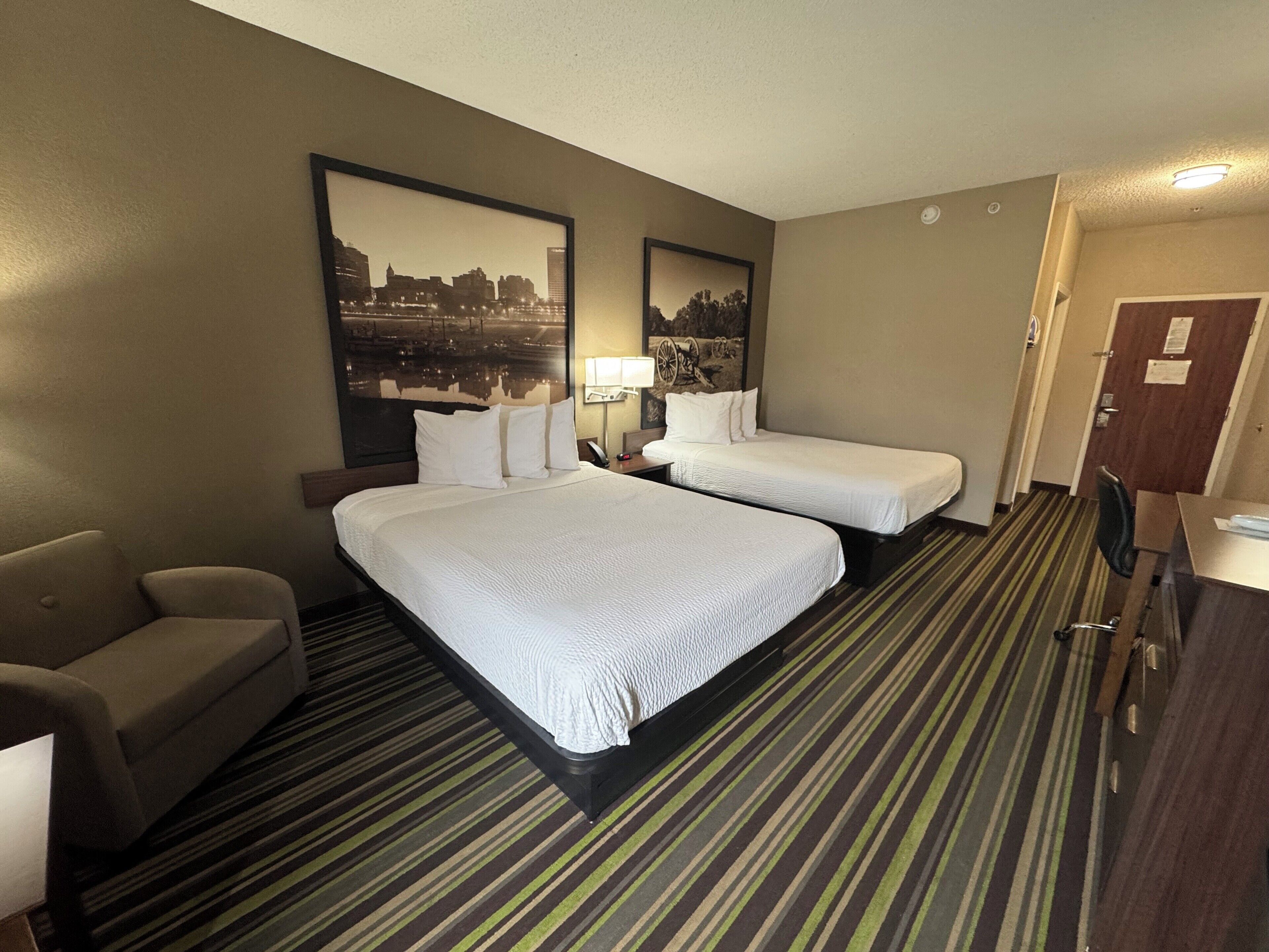 A hotel room with two beds, a sofa, a desk, and a mirror.