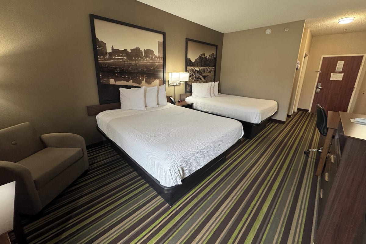 A hotel room with two beds, a sofa, a desk, and a mirror.