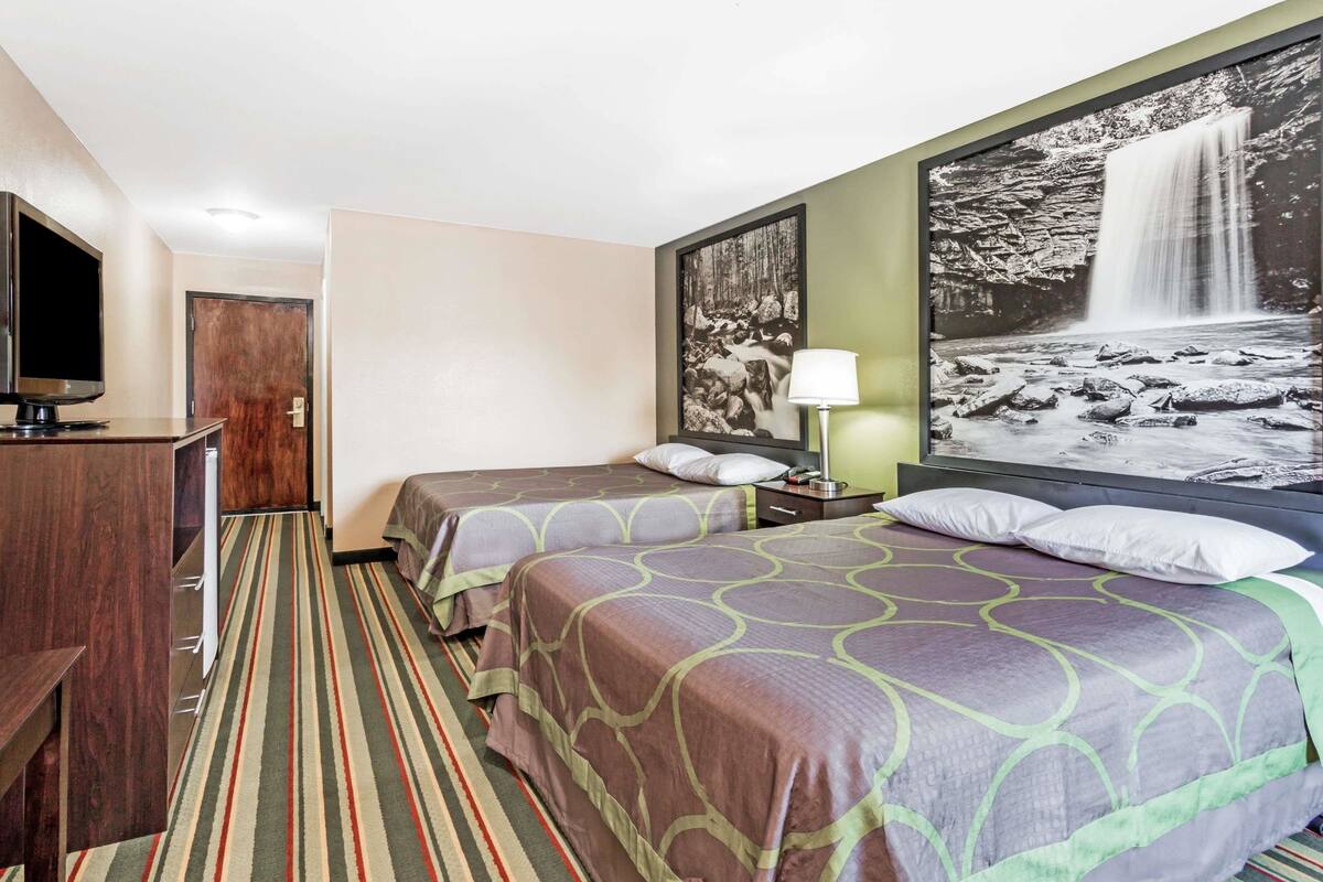 Habitación de hotel con dos camas, televisión, escritorio, lámpara y una pintura grande de una cascada en la pared.