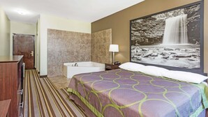 A hotel room with a large bed, a bathtub, a wooden cabinet, and a framed waterfall painting on the wall.
