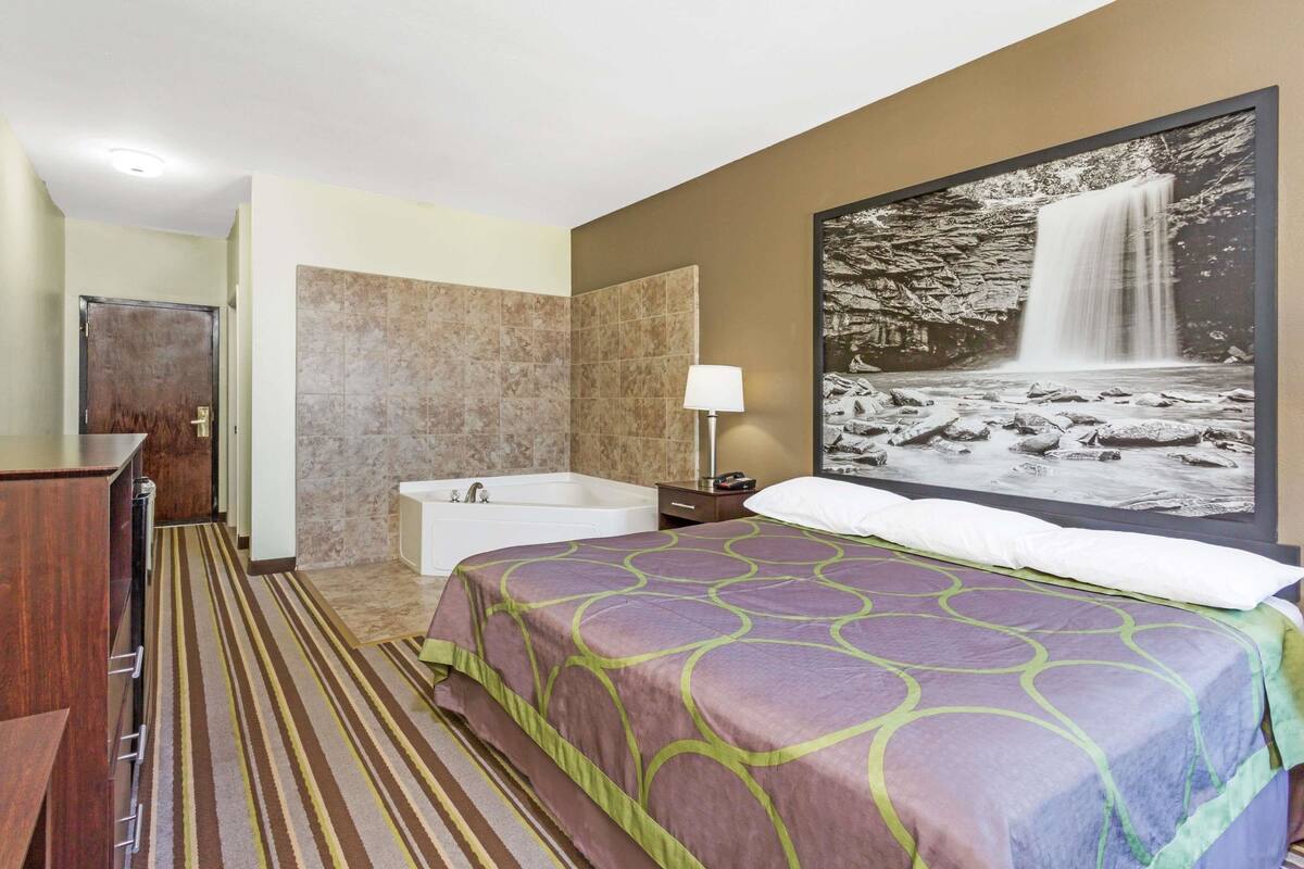 Una habitación de hotel con una cama grande, una bañera, un armario de madera y un cuadro de una cascada enmarcada en la pared.