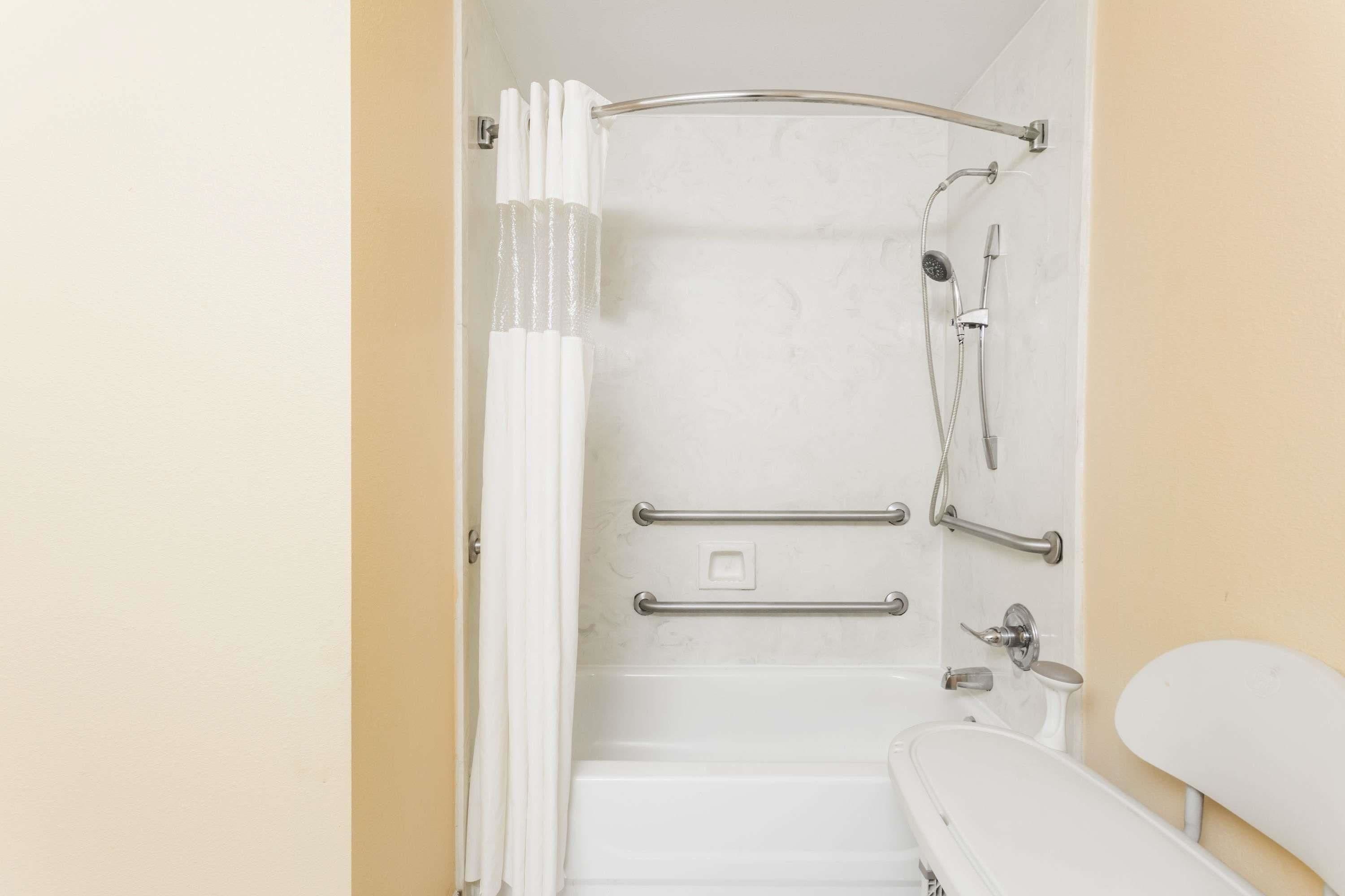 A bathroom with a bathtub, shower, and grab bars.