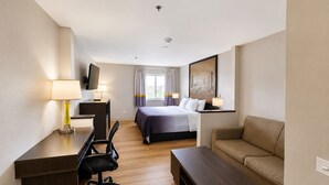 Habitación de hotel con cama, escritorio con silla, sofá, televisor y un cuadro en la pared.