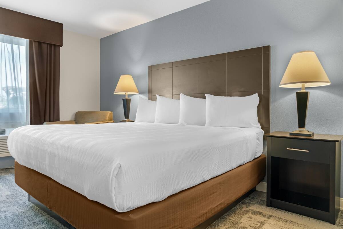 A hotel room with a large bed, two bedside tables with lamps, a chair, and a window with curtains.
