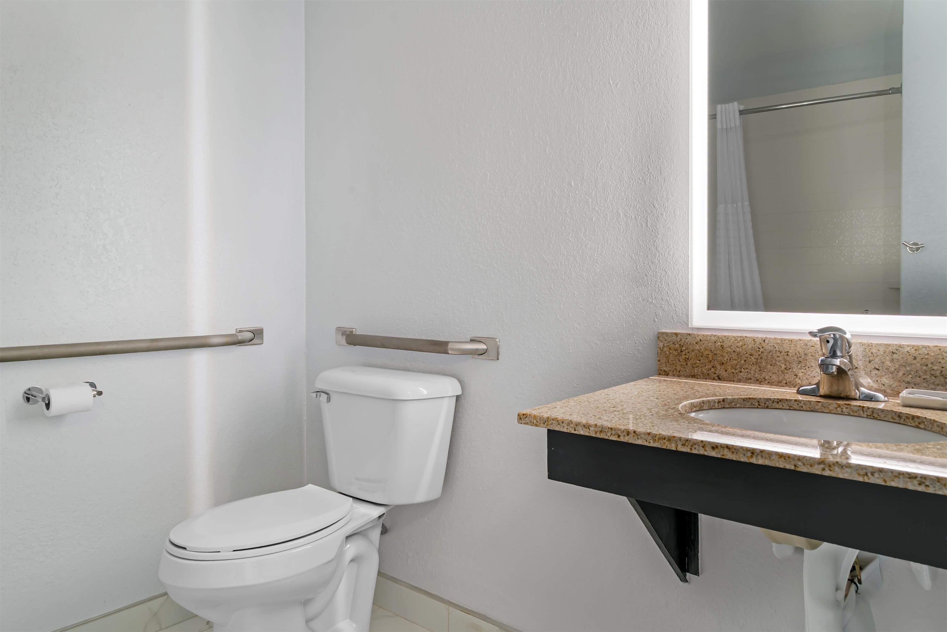 A bathroom with a white toilet, a sink with a granite countertop, and a shower area.