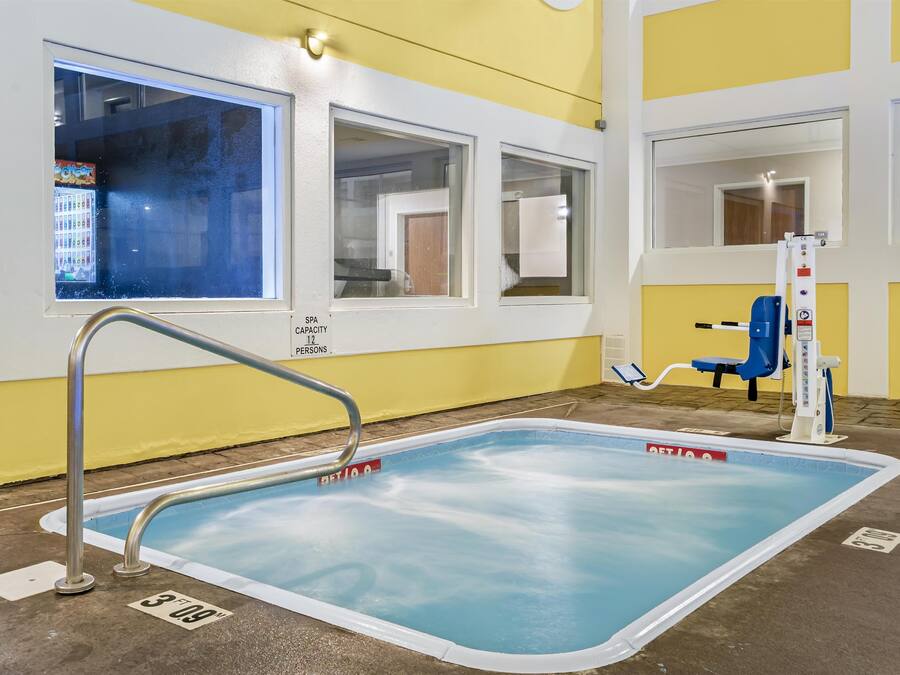 Una pequeña piscina interior con una escalera metálica, decoración azul y blanca y un letrero que indica una capacidad para 12 personas.