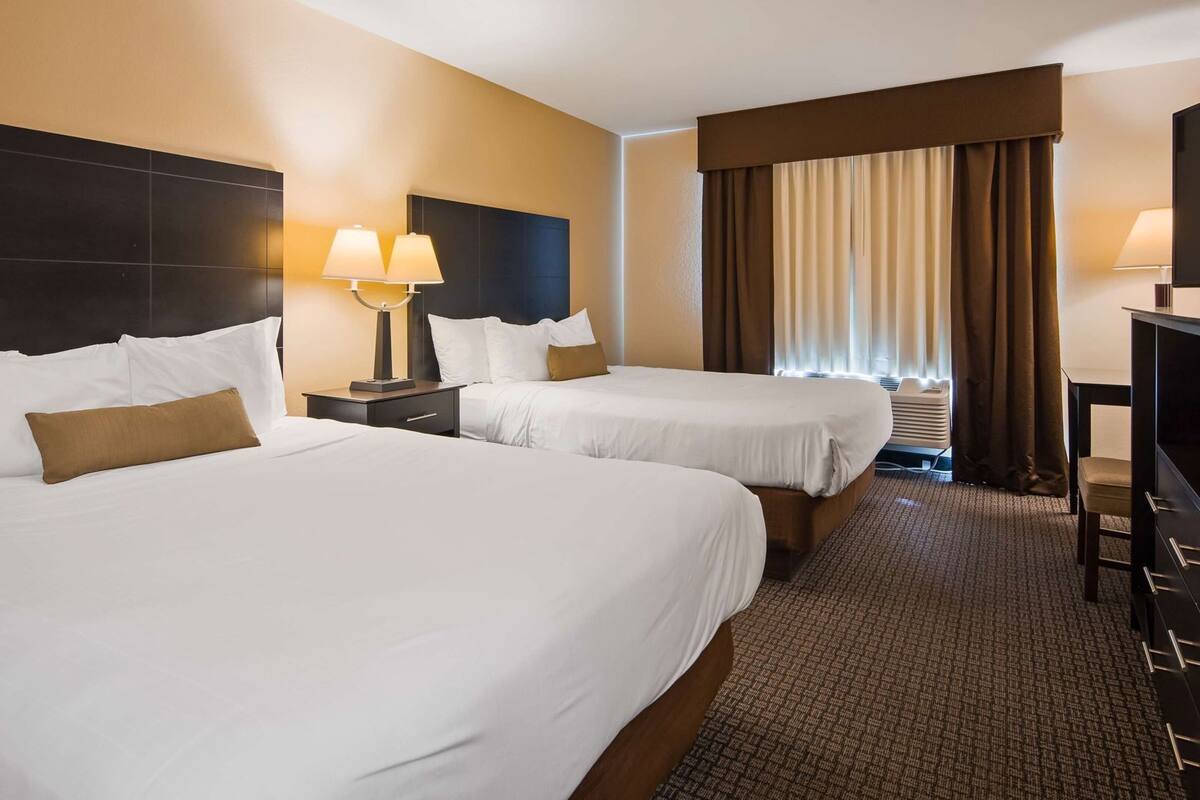 A hotel room with two beds, a desk, a television, and a window with curtains.