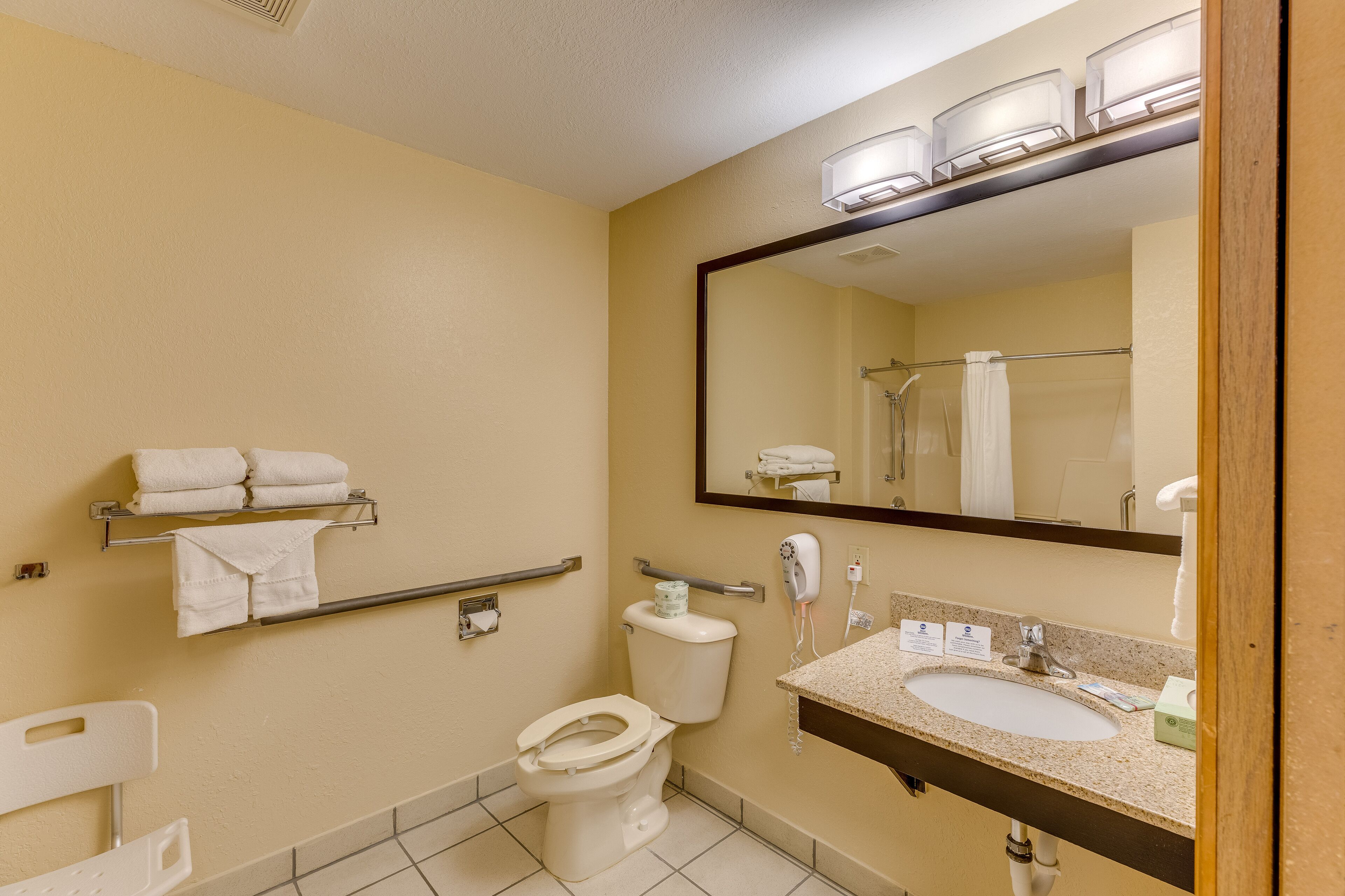 A standard hotel bathroom with a toilet, sink, mirror, towel rack, and hand dryer.