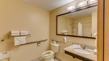 A standard hotel bathroom with a toilet, sink, mirror, towel rack, and hand dryer.