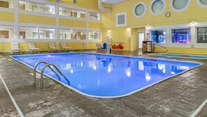 Une piscine intérieure à l’eau claire, entourée de chaises longues et bordée d’un mur jaune vif.