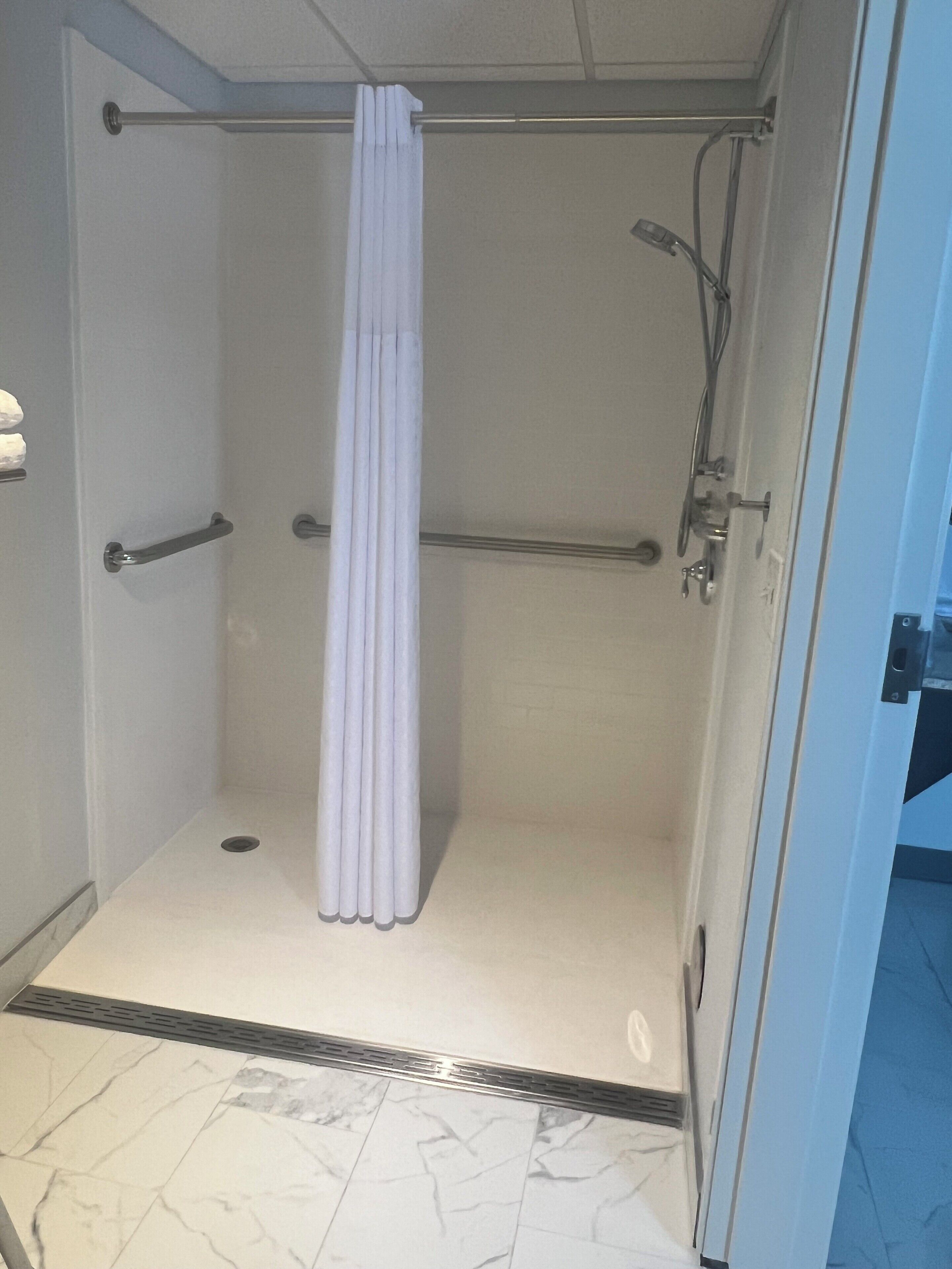 A walk-in shower with a white curtain, a grab bar, and a handheld showerhead.
