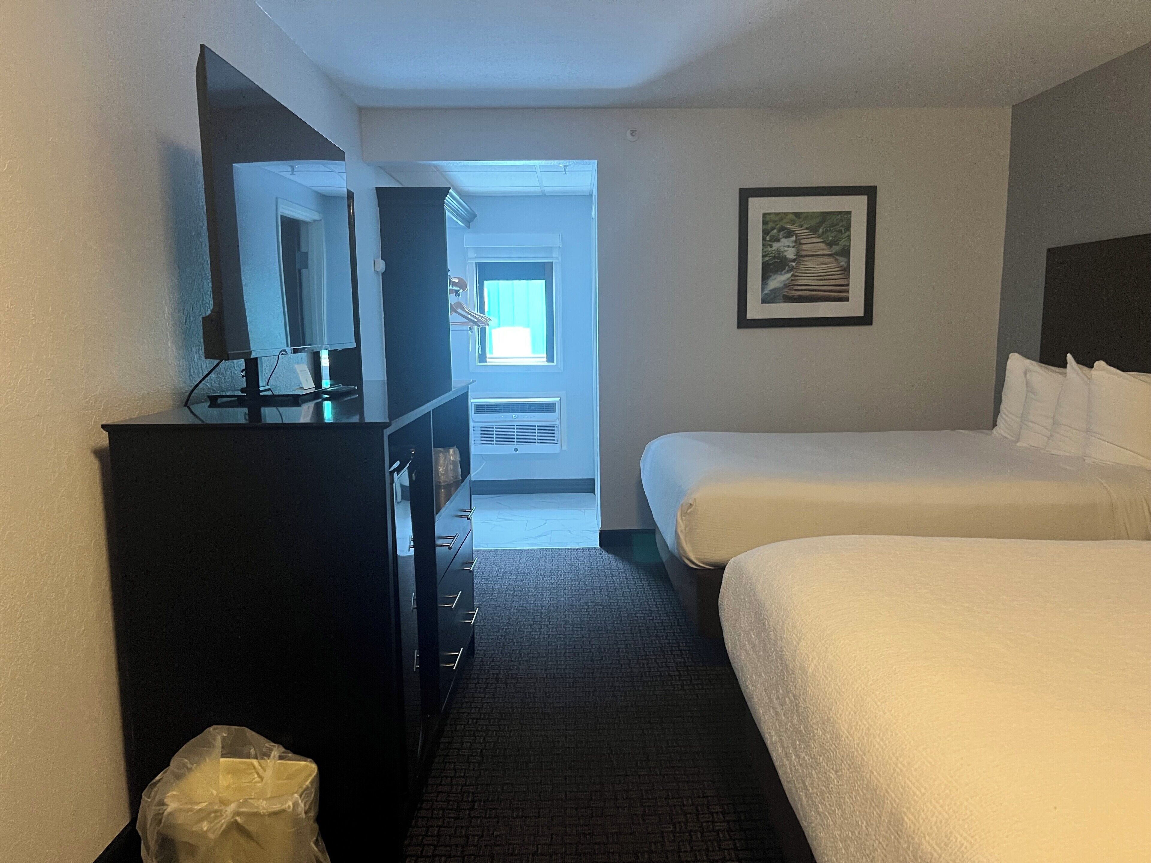 A hotel room with a bed, a dresser, a television, and a framed picture on the wall.