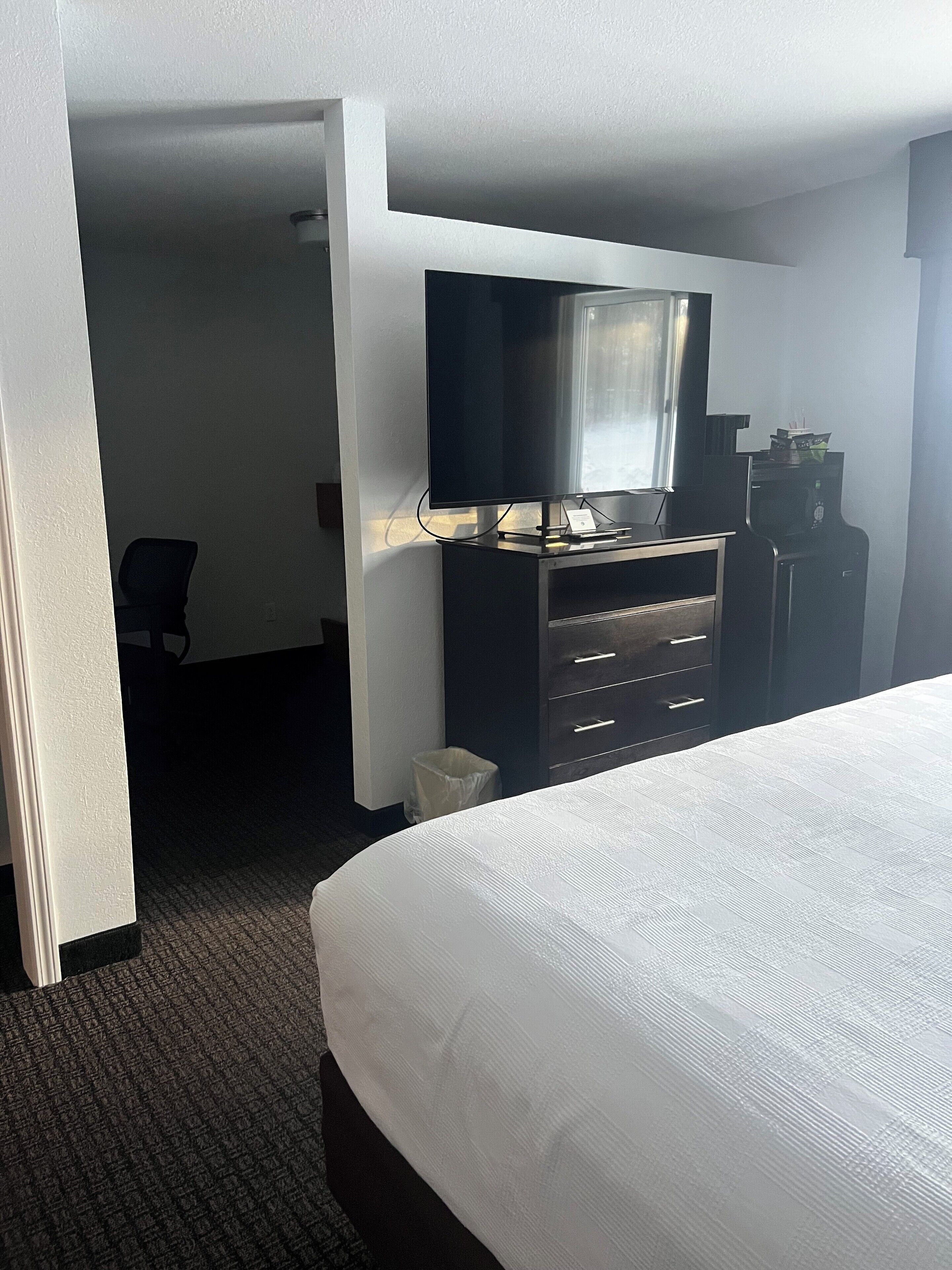 A hotel room with a bed, a dresser, a television, and a desk.