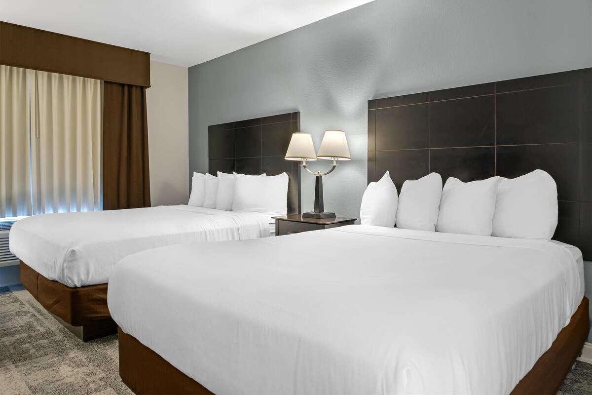 A hotel room with two beds, a nightstand with lamps, and a large window with curtains.