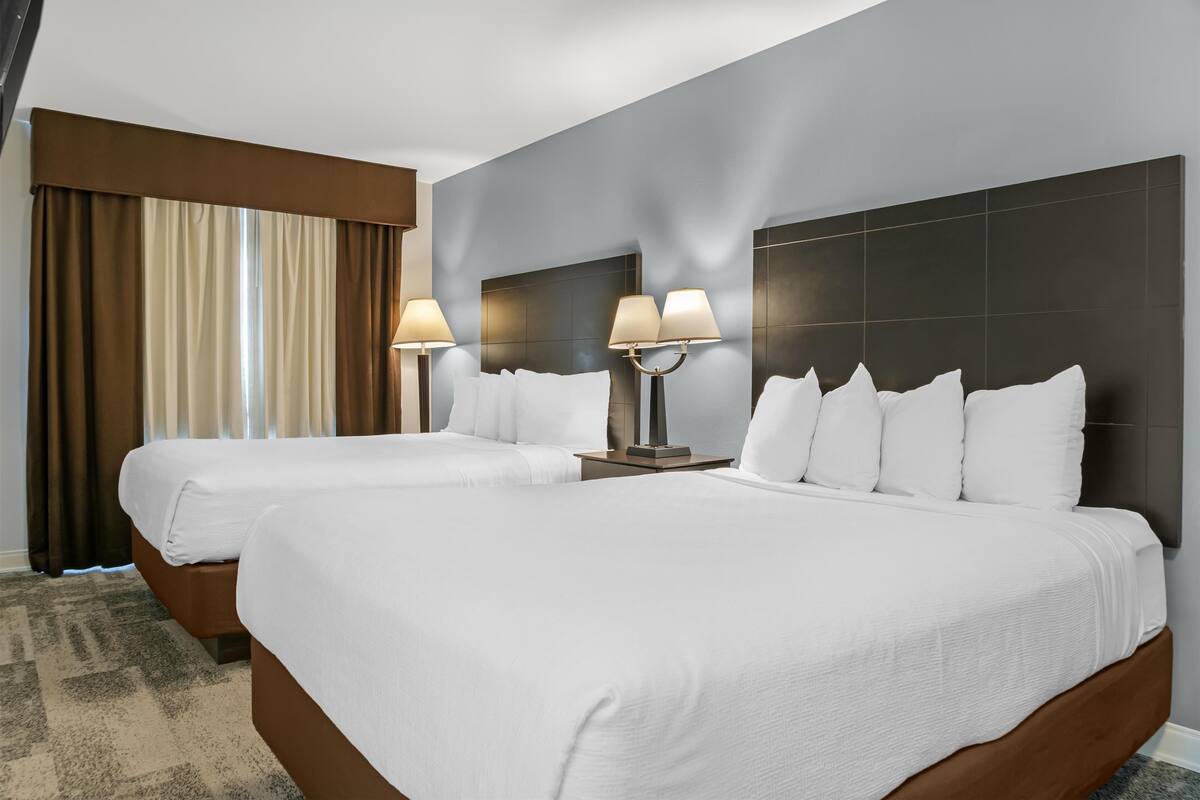A hotel room with two beds, a large window with curtains, and a dark tiled wall.