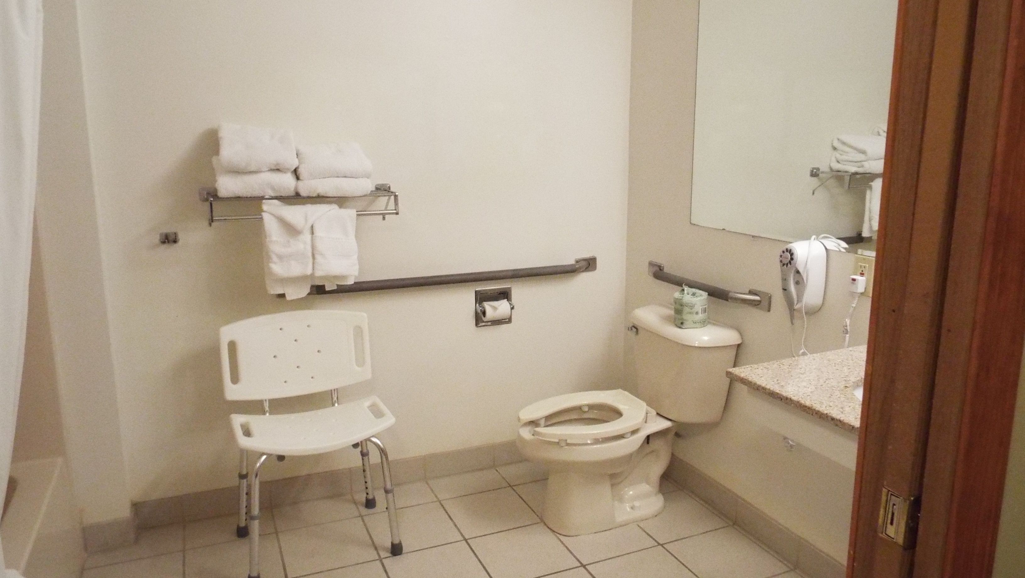 Een kleine badkamer met een toilet, een witte stoel, een handdoekhouder en een handdroger.