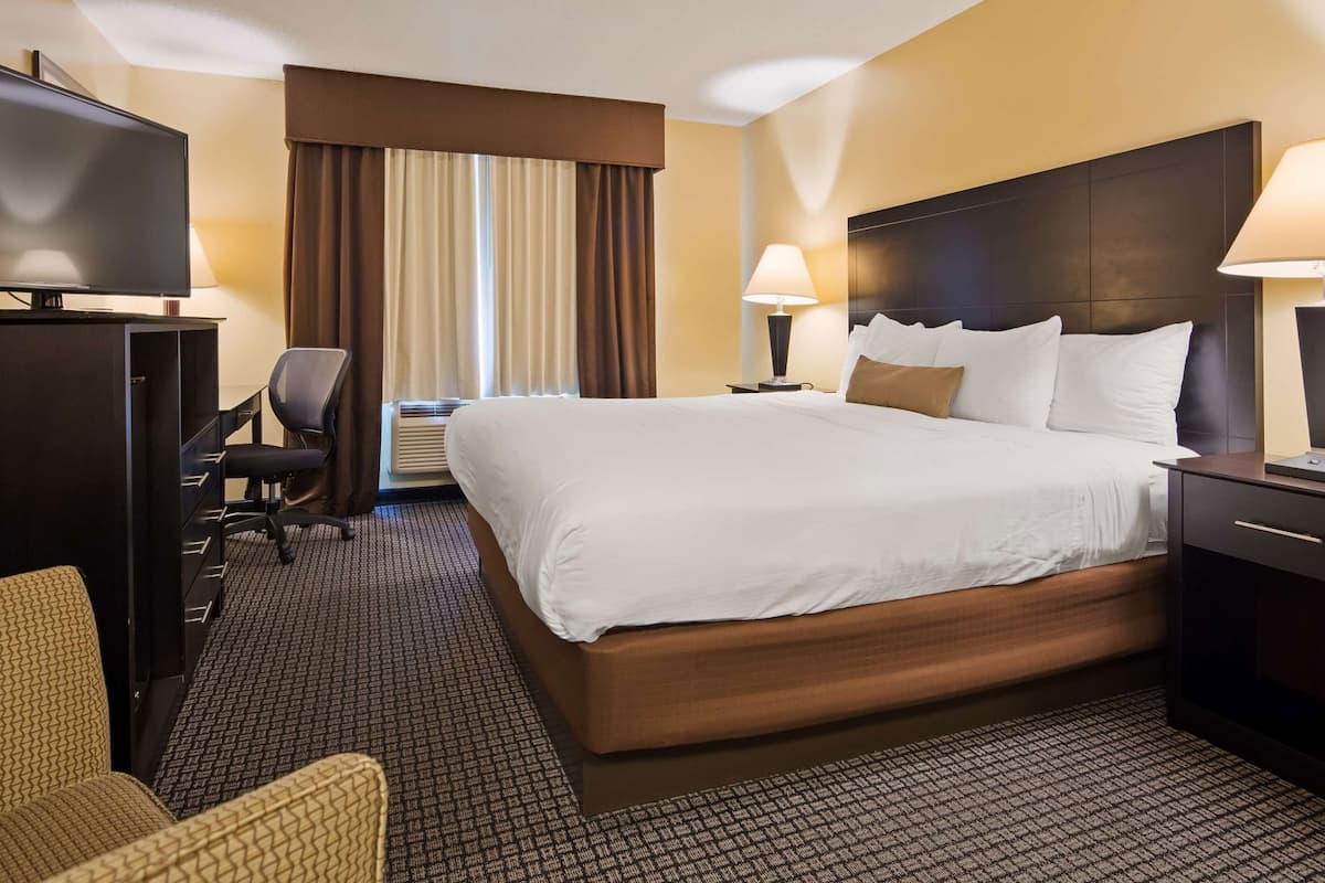 A hotel room with a large bed, two bedside tables with lamps, a desk with a chair, a television, and a window with curtains.