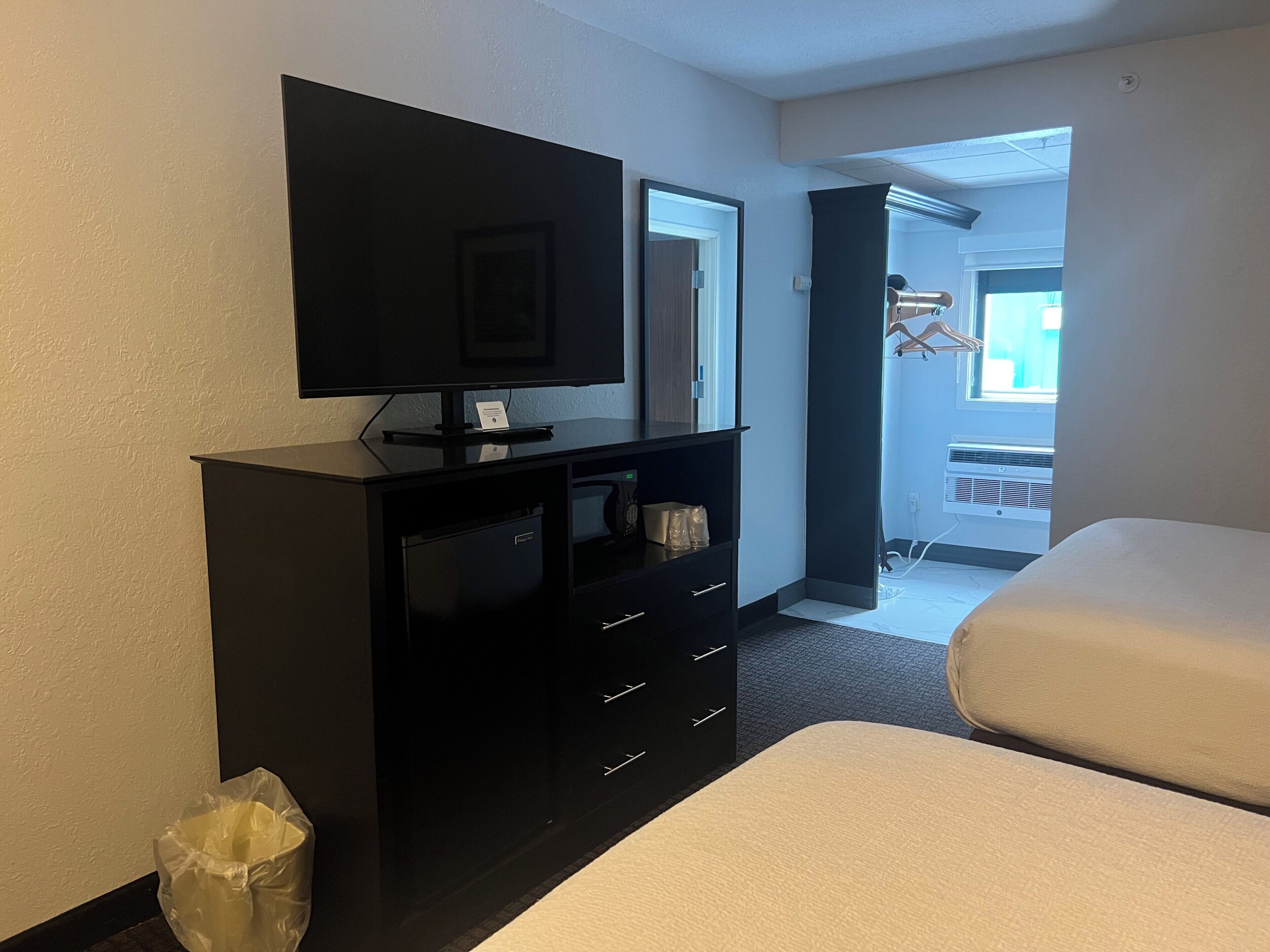 Ein Hotelzimmer mit Fernseher auf einem schwarzen Schrank, einem kleinen Schreibtisch mit Schubladen, einem Mülleimer und zwei Betten.
