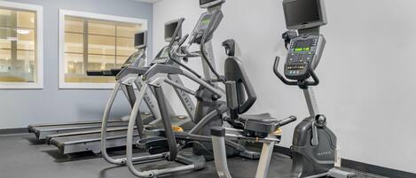 A row of treadmills with digital displays, a window with blinds, and a grey floor.