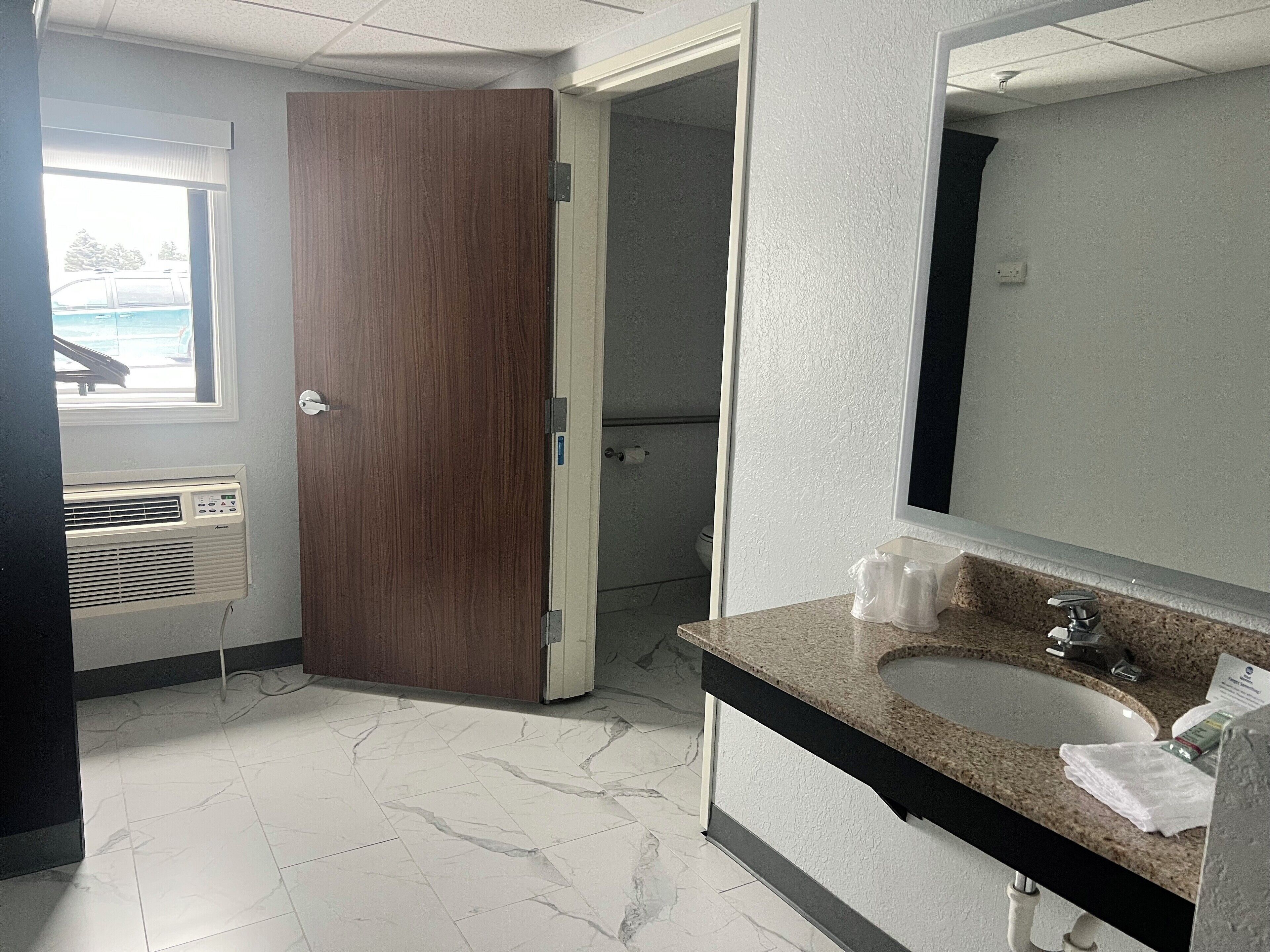 A bathroom with a marble floor, a sink with a granite countertop, a mirror, and a wooden door.