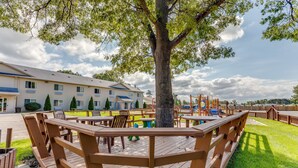 Une terrasse en bois avec des tables de pique-nique et un grand arbre au centre.