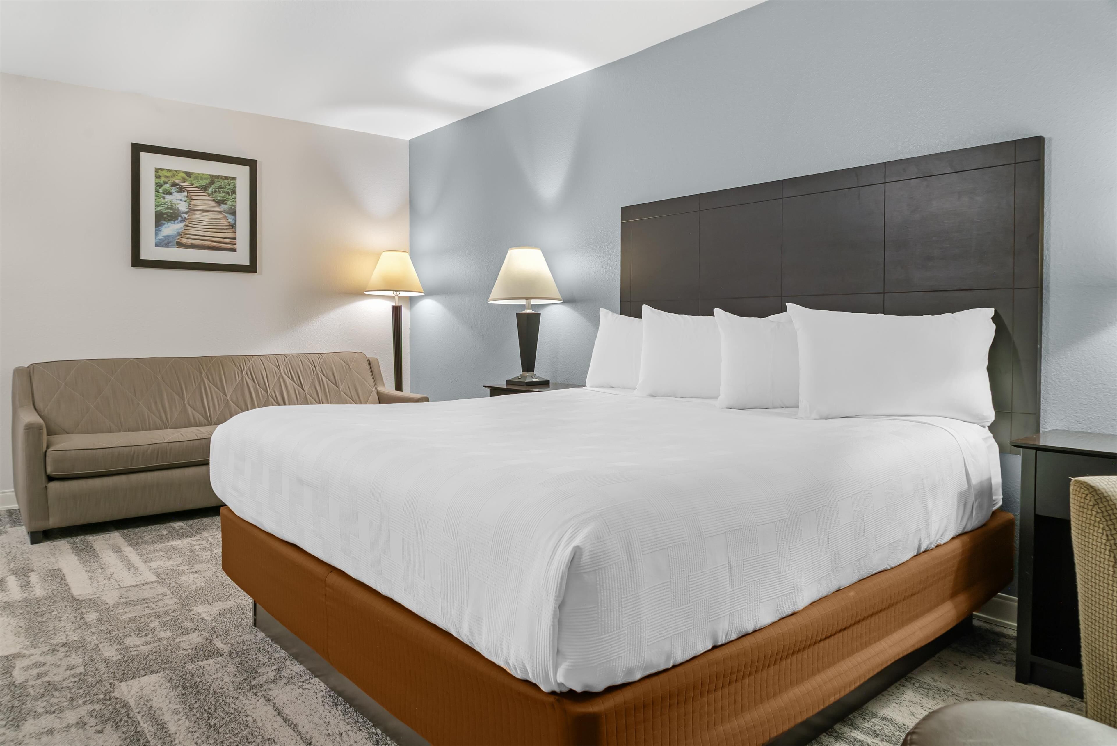 A hotel room with a large bed, a sofa, two bedside lamps, and a framed picture on the wall.