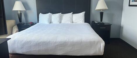 Une chambre d’hôtel avec un grand lit, deux tables de chevet avec des lampes, une horloge et un tableau encadré au mur.