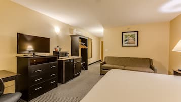 Habitación de hotel con cama, televisor, escritorio con cajones, microondas, armario, sofá y un cuadro en la pared.