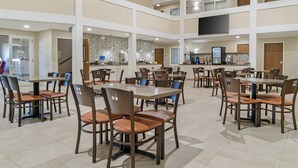 Un grand espace dédié à la salle à manger, avec plusieurs tables et chaises, une cuisine à l’arrière-plan et un plafond haut doté d’un éclairage encastré.