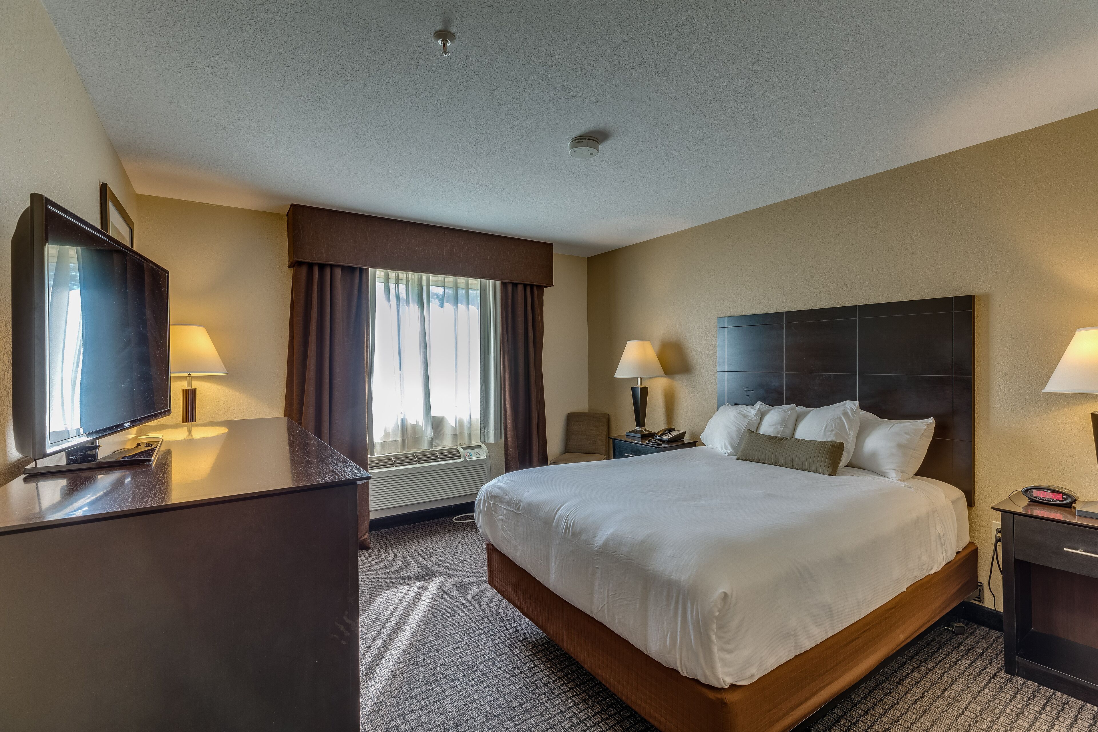 A hotel room with a large bed, two bedside tables with lamps, a television on a desk, and a window with curtains.