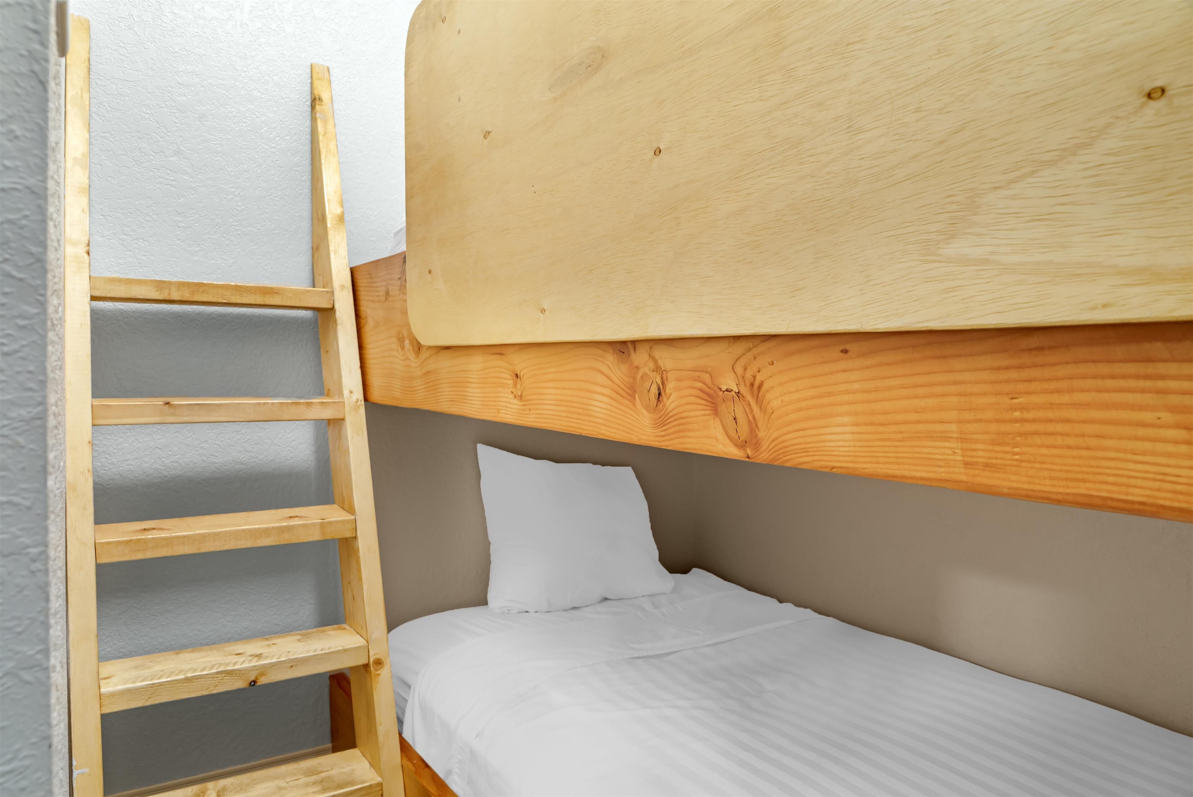 A bunk bed with a wooden ladder, a white pillow, and a grey wall.