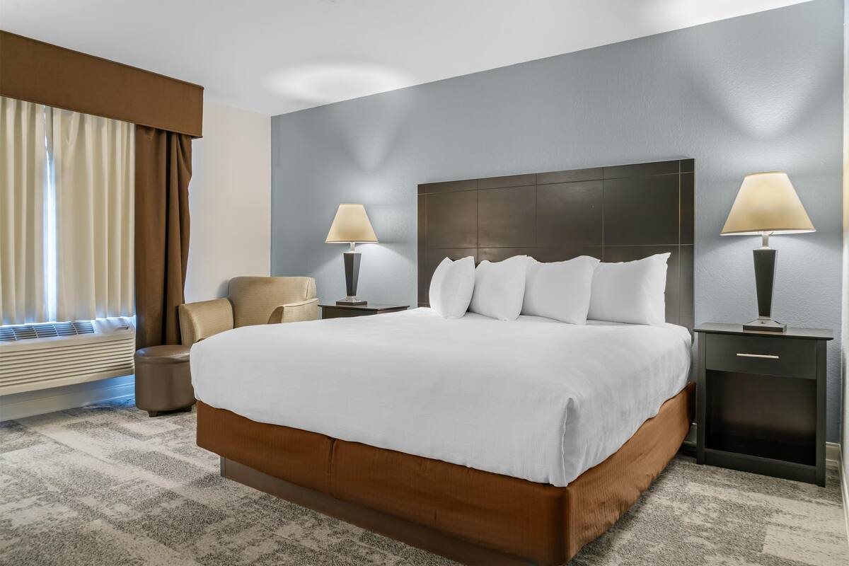 A hotel room with a large bed, two bedside tables with lamps, a chair, and a window with curtains.