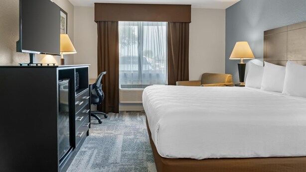 Une chambre d’hôtel avec un grand lit, un bureau avec un ordinateur, une télévision et deux lampes.