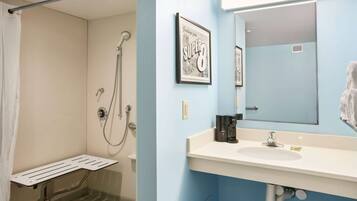 A bathroom with a shower, a sink, a mirror, and a framed picture on the wall.