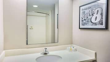 A bathroom with a white sink, a large mirror, and a framed picture of a road on the wall.