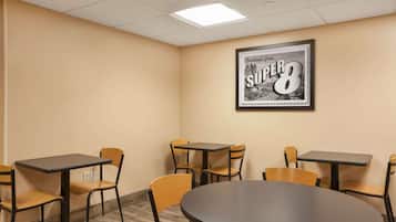 A conference room with a large round table and four rectangular tables, each with two chairs. A framed picture of 'Greetings from Super 8' is on the wall.