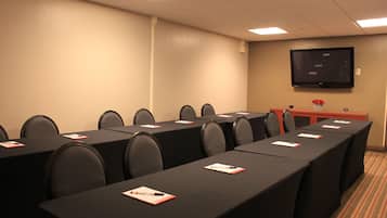 A conference room with multiple tables, chairs, and a television on the wall.