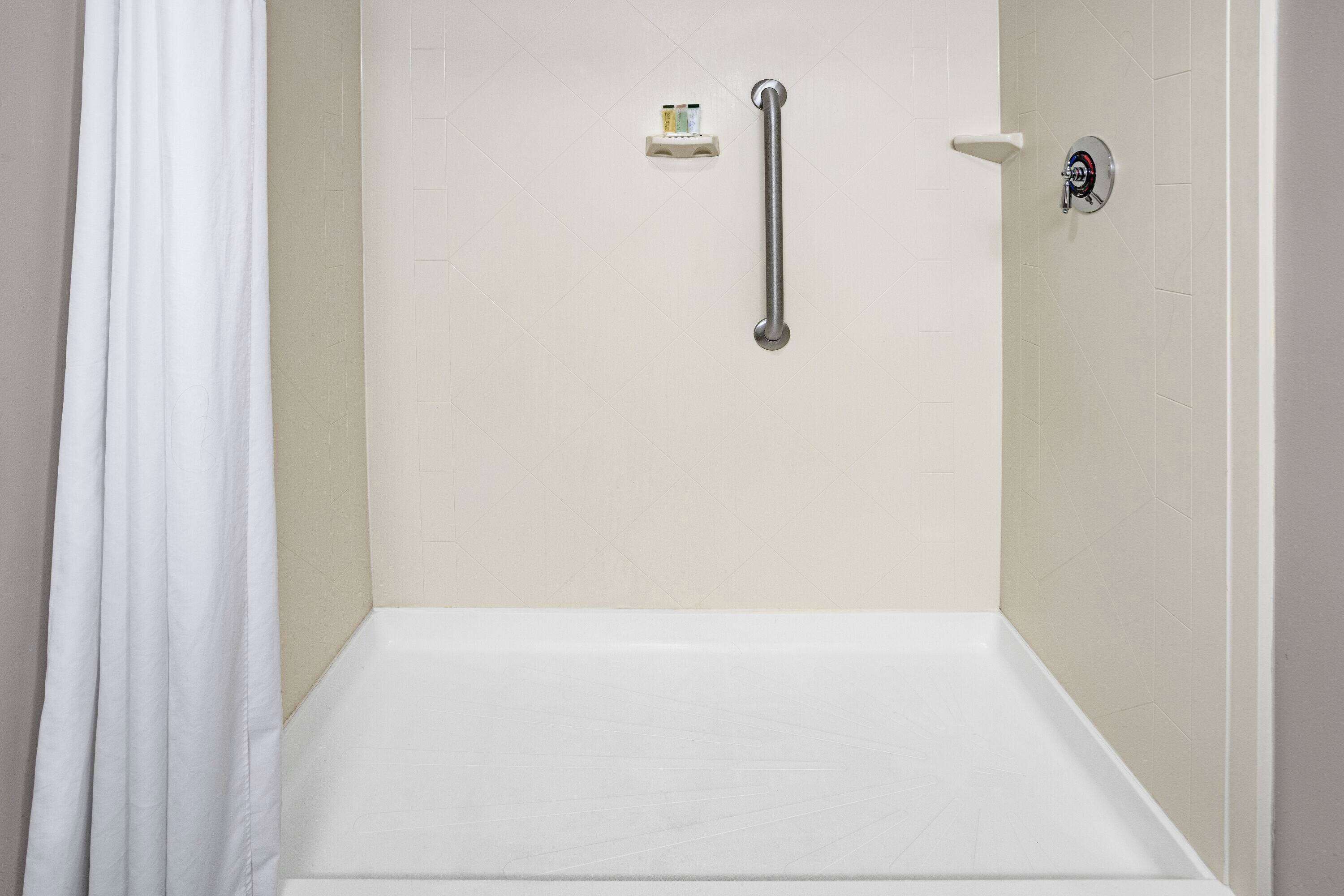 A shower area with a white bathtub, a grab bar, and a soap dish on the wall.