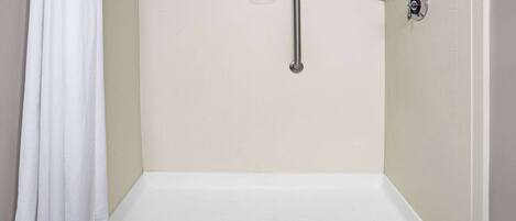 A shower area with a white bathtub, a grab bar, and a soap dish on the wall.