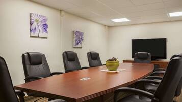 A conference room with a long wooden table, black leather chairs, and two purple flower paintings on the wall.