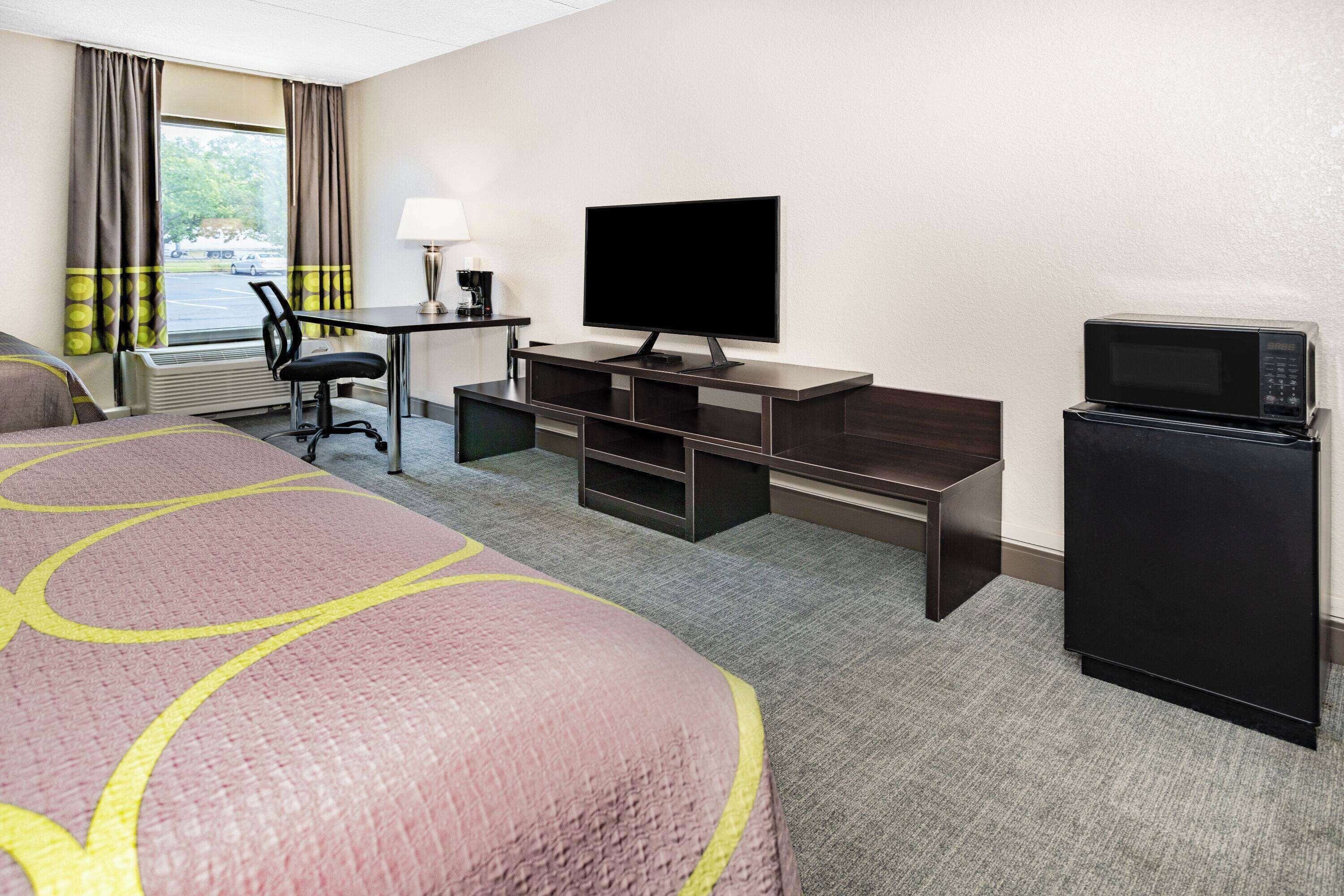 A hotel room with a bed, a desk with a television, a microwave, and a chair.
