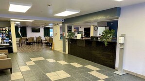Zona de recepción con mostrador de entrada, sillas, máquina expendedora y un reloj en la pared.