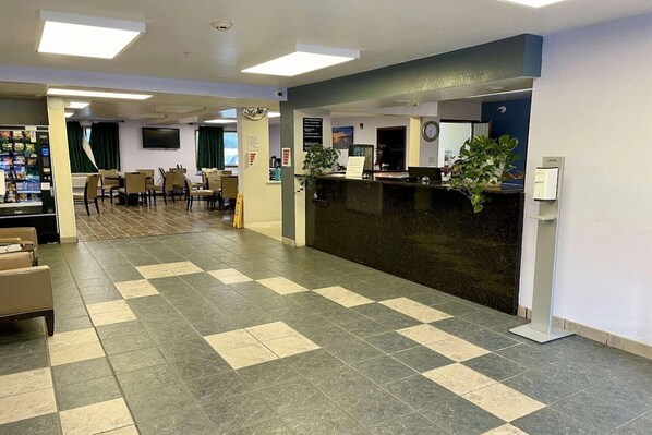 A reception area with a check-in counter, chairs, a vending machine, and a clock on the wall.