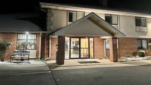 Un edificio de dos pisos con fachada de ladrillo, un porche cubierto y una banca en el exterior.