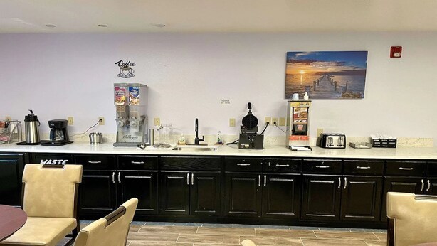 Una cocina moderna con estación de café, un cubo de basura y un cuadro de un atardecer.