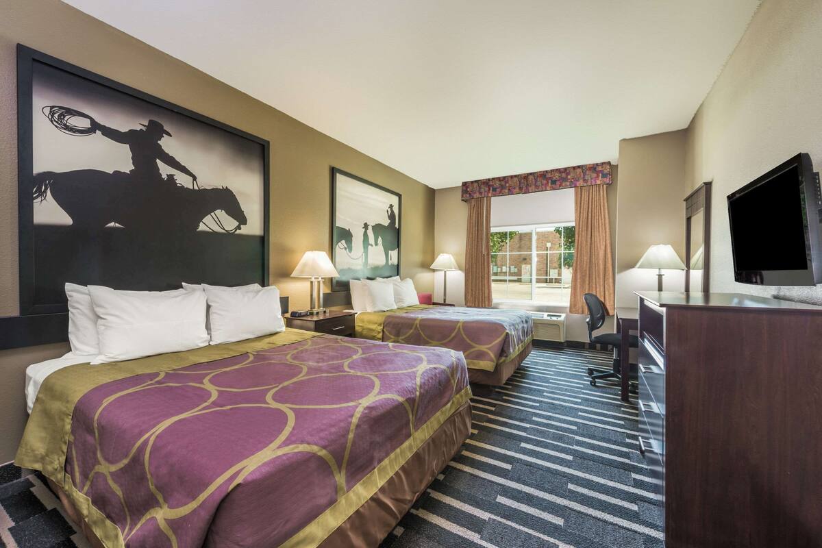 A hotel room with two beds, a desk, a TV, and artwork on the walls.